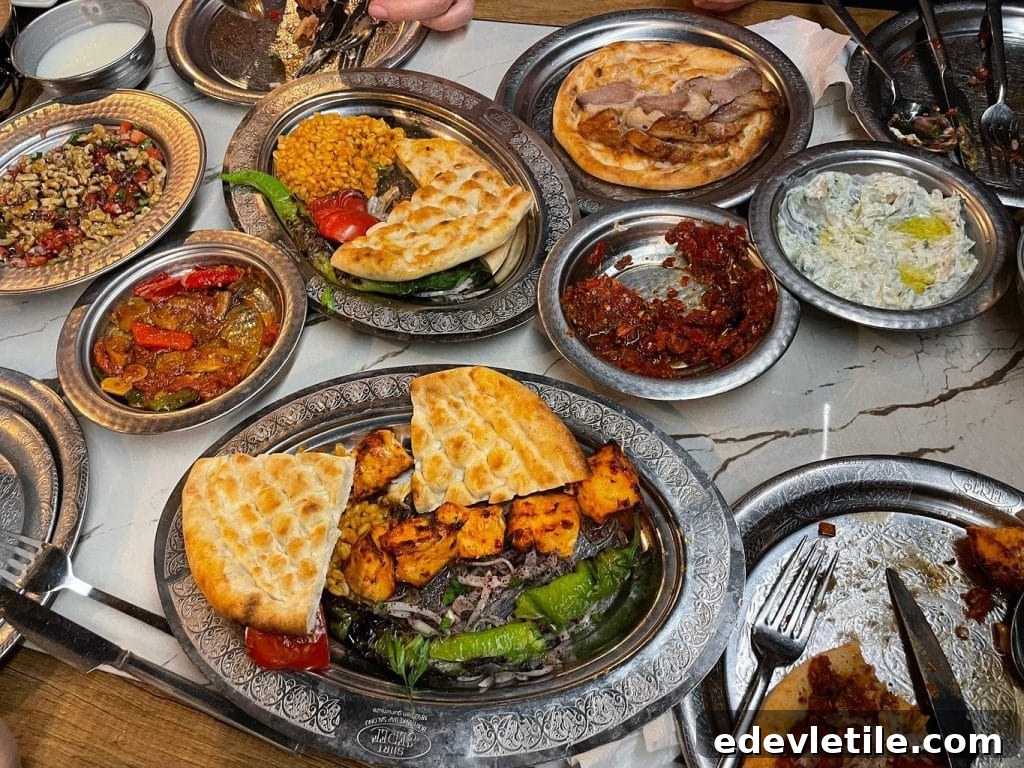 An overhead shot of a table filled with Turkish dishes including grilled meat, bulgur, flatbread, spicy tomato salad, eggplant stew, and meze, all served on traditional silver plates.
