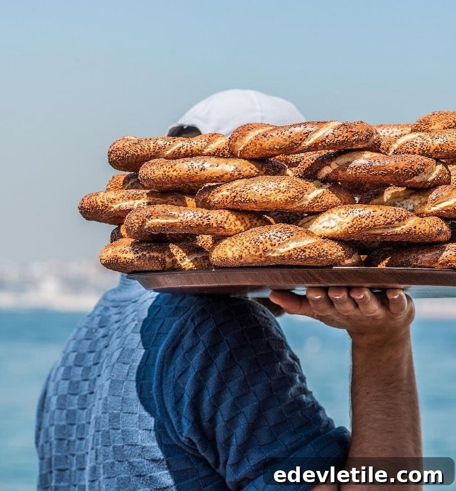 A street vendor in Istanbul balances a large tray of freshly baked simit (sesame-covered bread rings) on his shoulder, with the Bosphorus in the background.