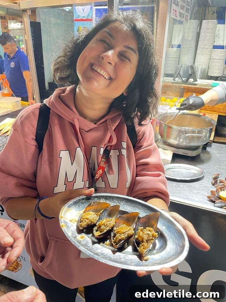 A cheerful woman tour guide in a pink hoodie holds a silver tray of midye dolma (stuffed mussels) at a street food stall in Istanbul during a street food tour