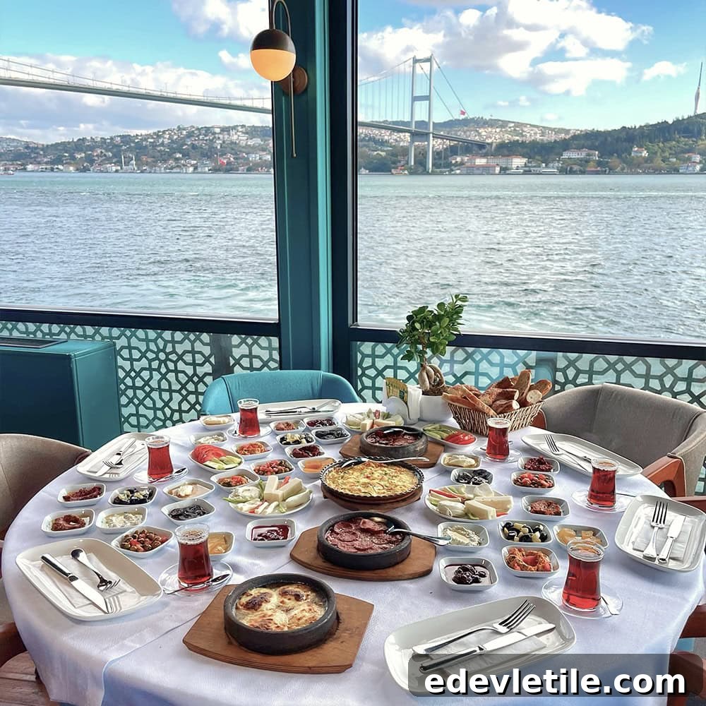A round table set with a full Turkish breakfast overlooking the Bosphorus, featuring dozens of small dishes, tea glasses, and a view of the Bosphorus Bridge through large windows.