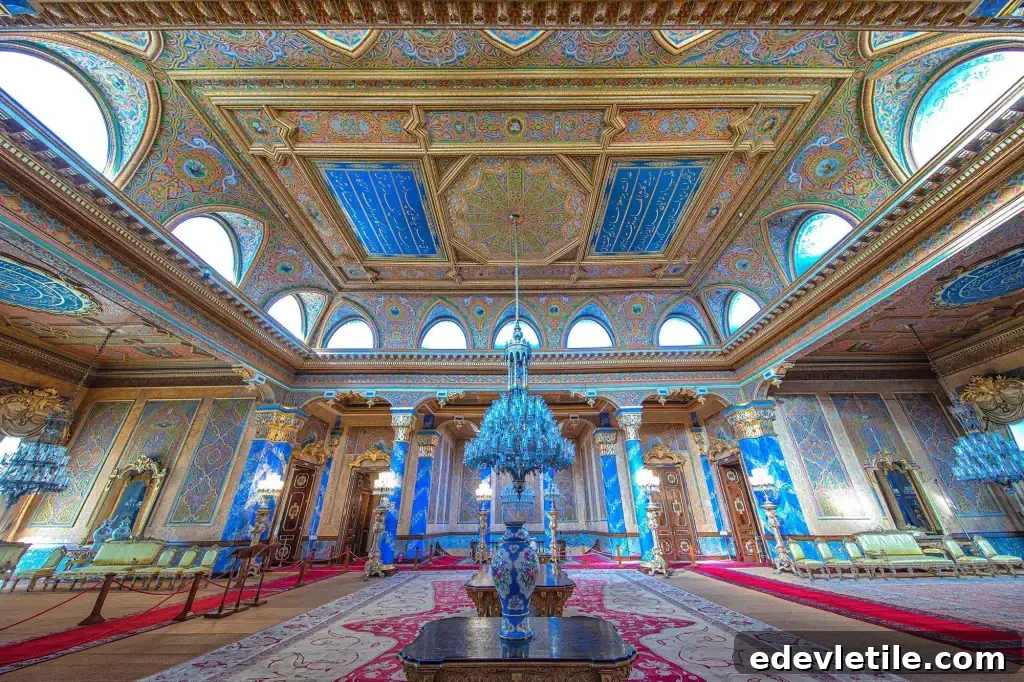 Lavish interior room in Beylerbeyi Palace with arched stained-glass windows, intricate ceiling designs in blue and gold, crystal chandeliers, and richly patterned rugs.