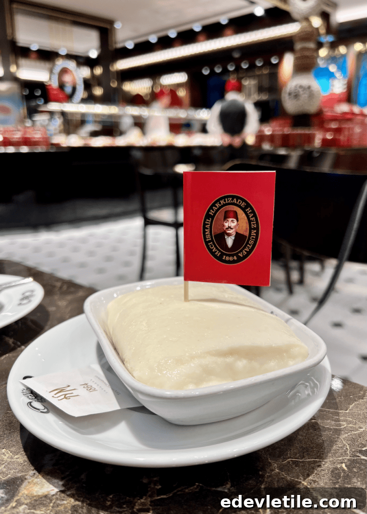Close-up of a creamy Turkish dessert called tavukgogsu served in a white dish at Hafız Mustafa inside Galataport Istanbul, topped with a small red flag featuring the brand’s historic logo.