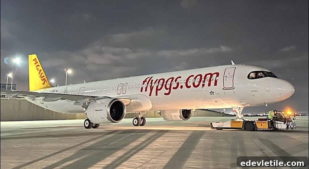 Pegasus Airlines jet with yellow tail and “flypgs.com” branding, parked on a runway under night lights, preparing for departure.